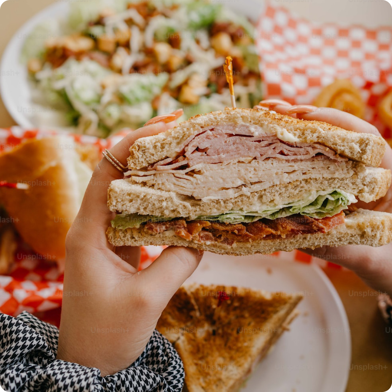 Hands holding a layered deli club sandwich